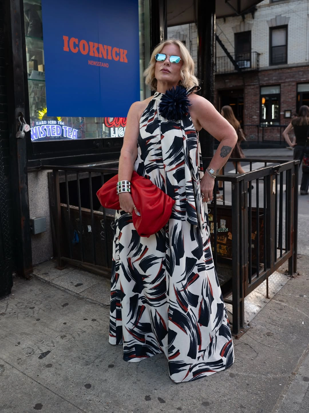 Woman in printed maxi dress holding red clutch outside