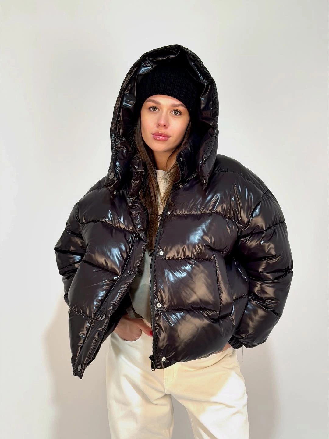 Glossy black hooded puffer with beanie and cream trousers