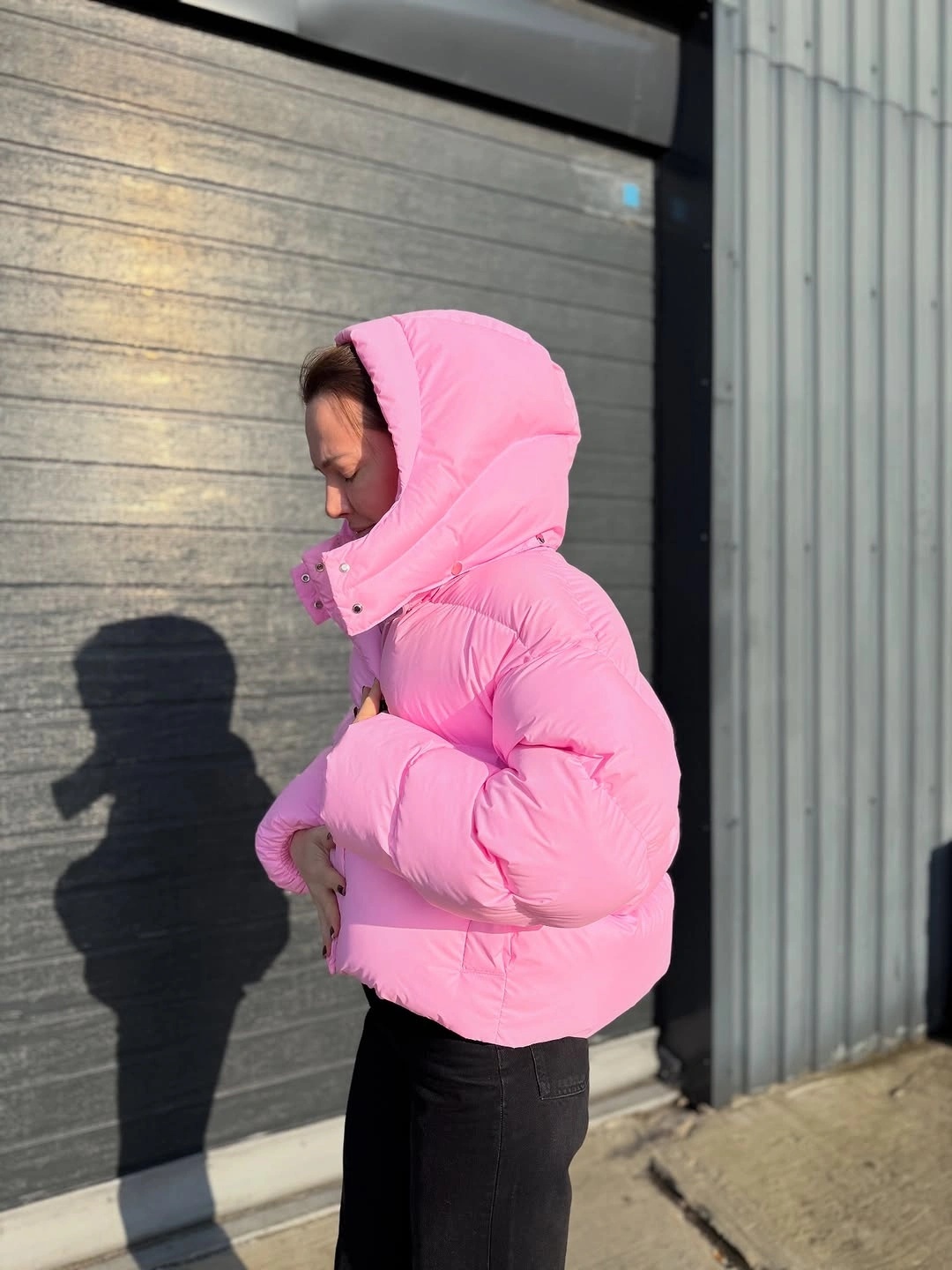 Bright pink hooded puffer with black pants in side view