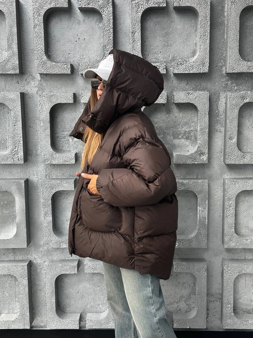 Dark brown hooded puffer with cap, sunglasses, and light jeans