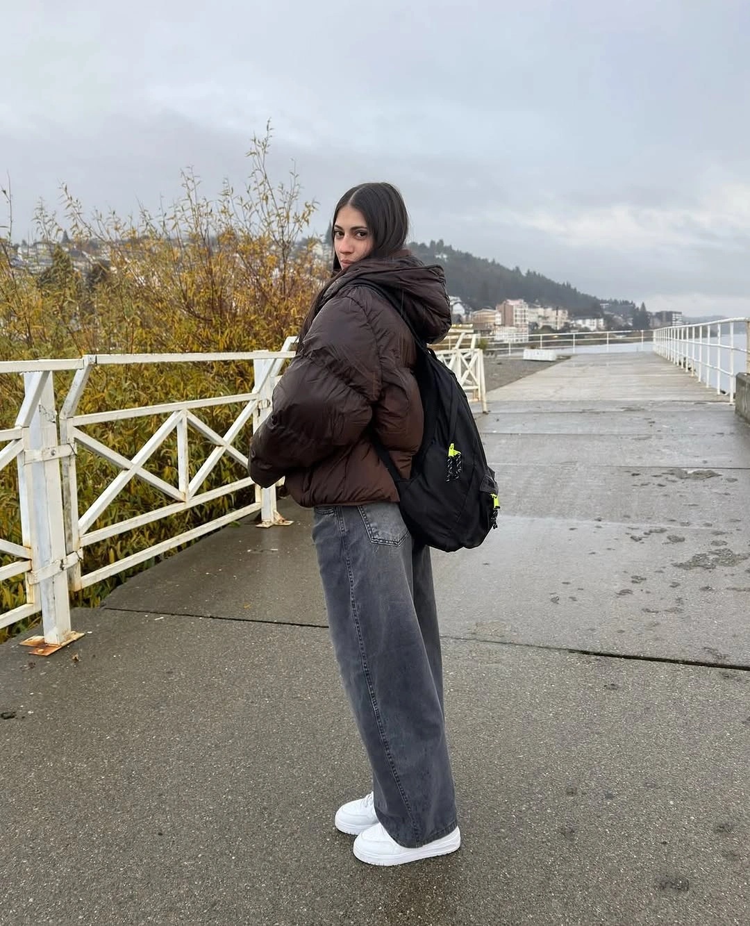 Dark brown puffer with backpack, gray jeans, and white sneakers