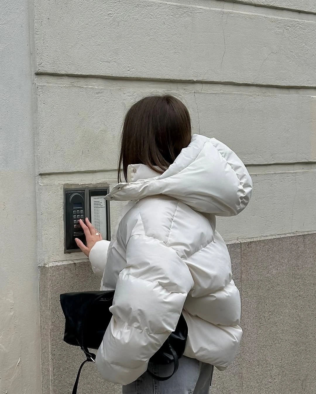 White oversized hooded puffer seen from side with black bag