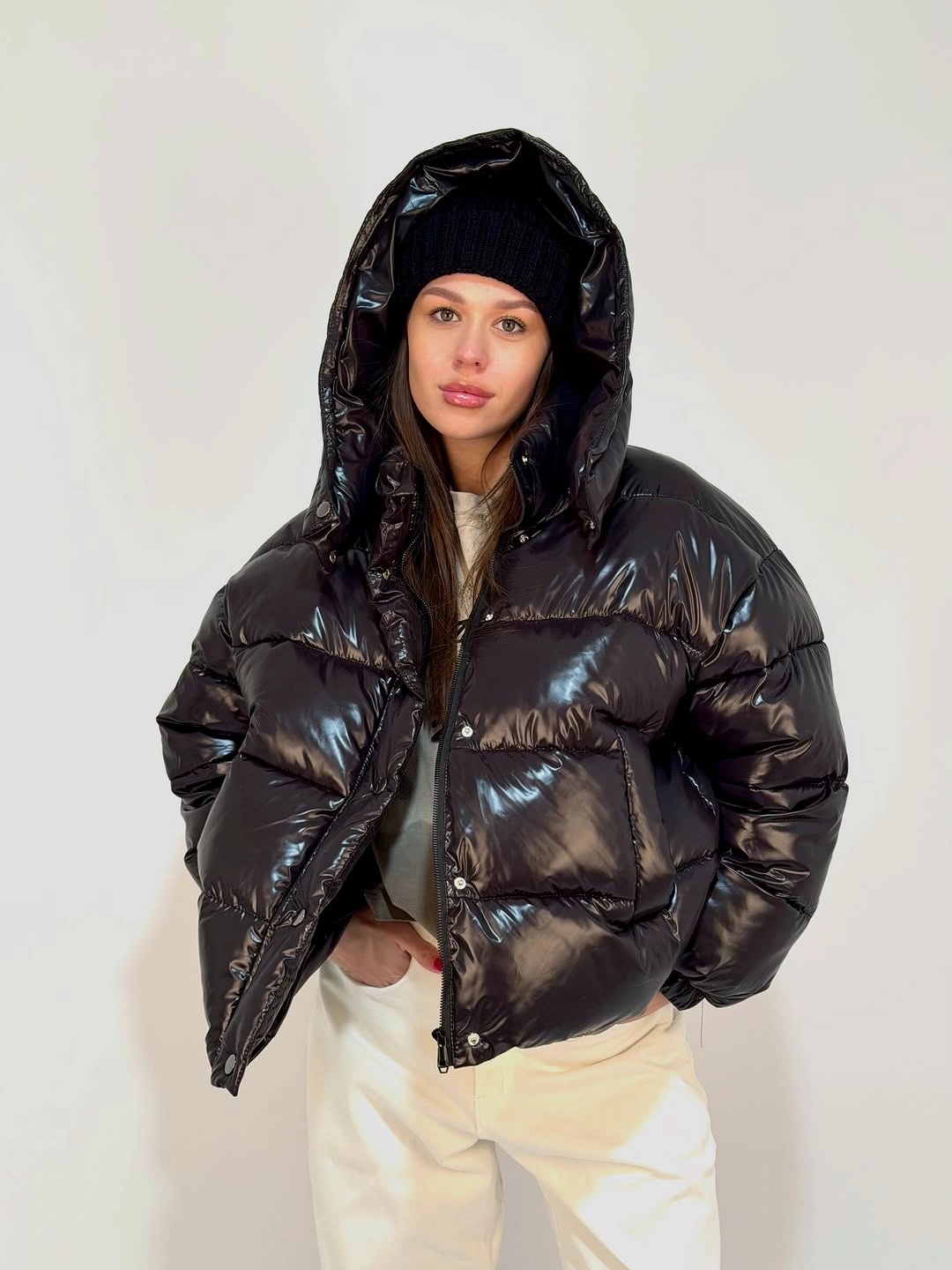 Glossy black hooded puffer with beanie and cream trousers