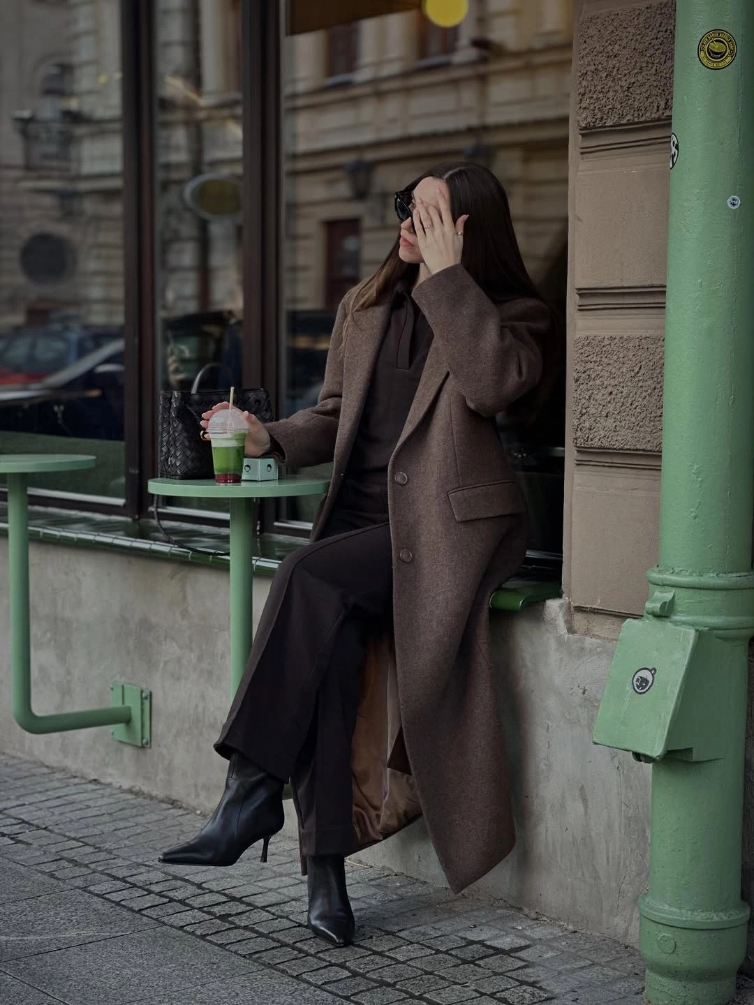 Long brown coat with dark wide trousers and pointed boots