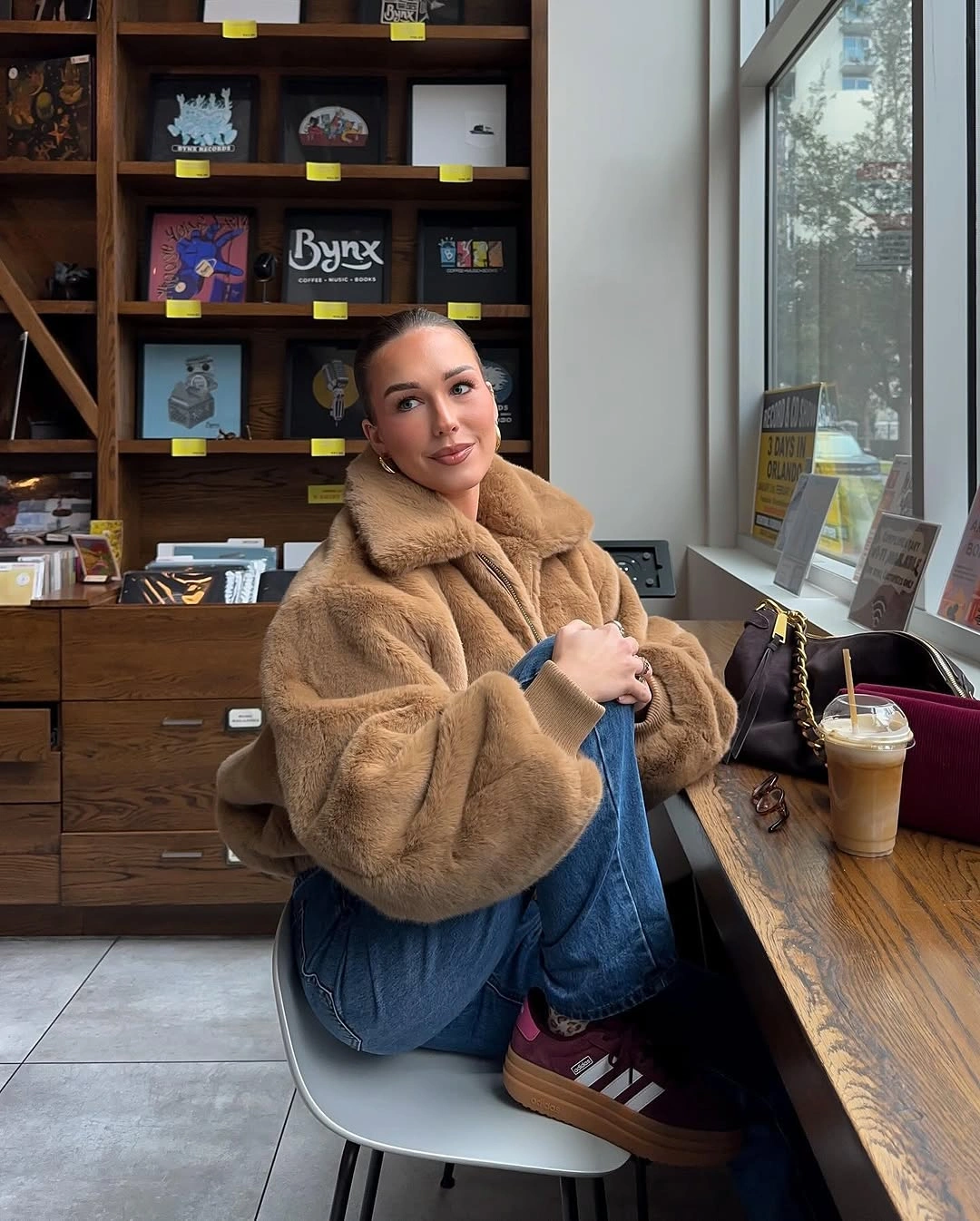 Tan plush jacket with jeans and burgundy sneakers indoors