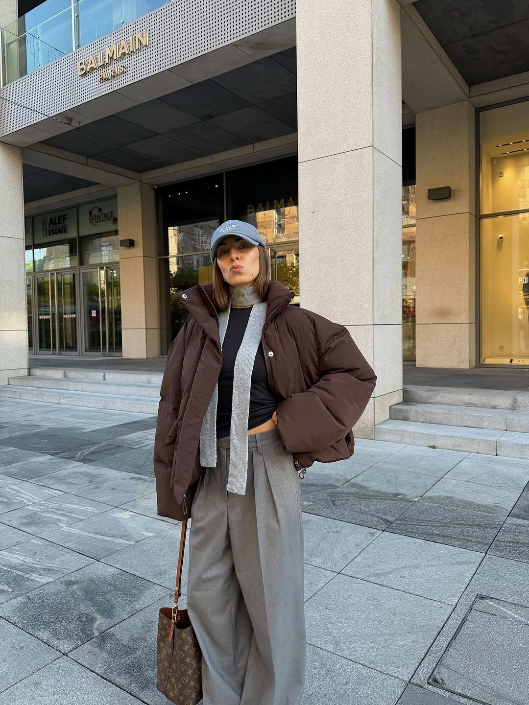 Brown puffer with gray trousers, blue cap and patterned bag