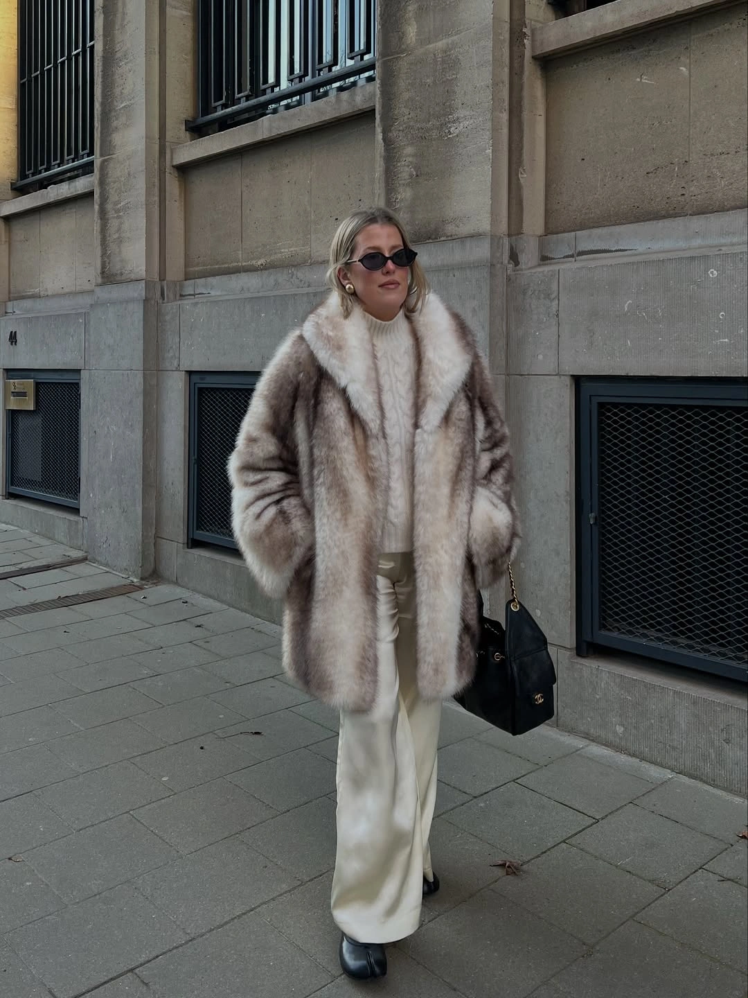 Plush taupe long coat with white wide trousers and black handbag