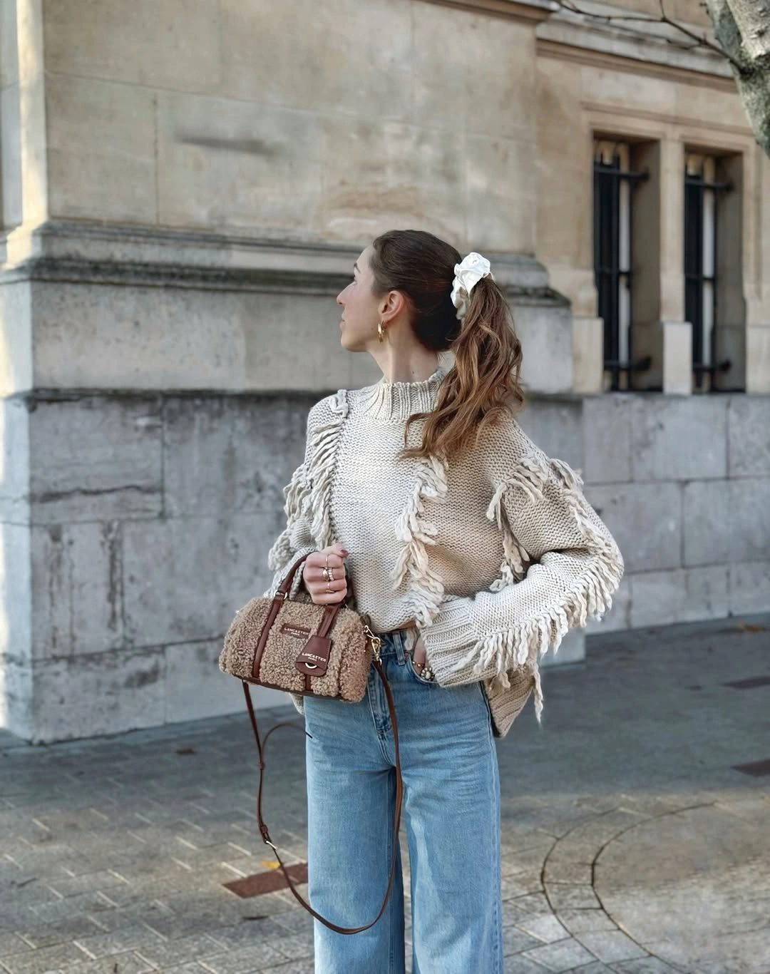 Cream fringed knit layer with light blue wide jeans and tan bag