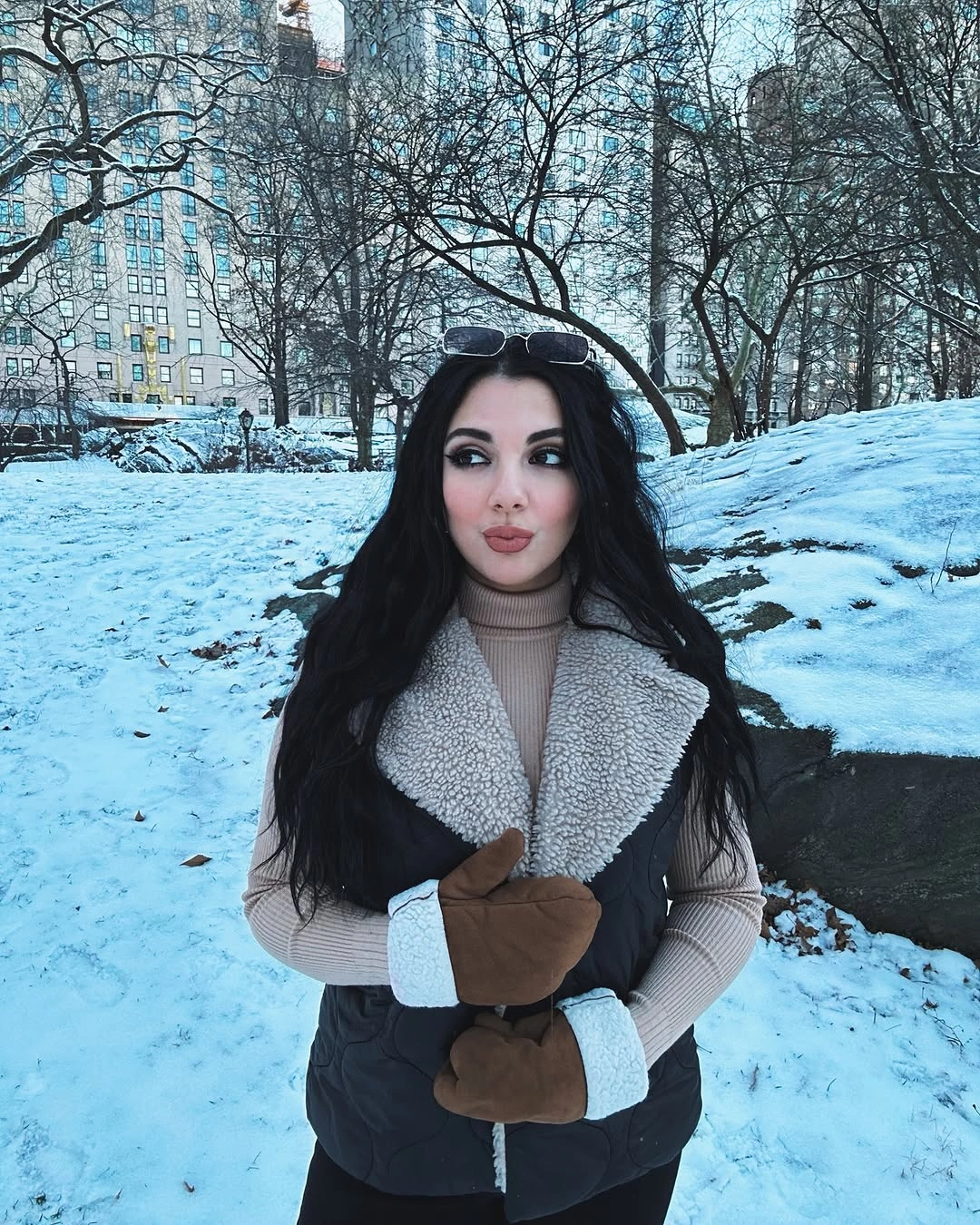 Black padded vest over taupe turtleneck with brown mittens