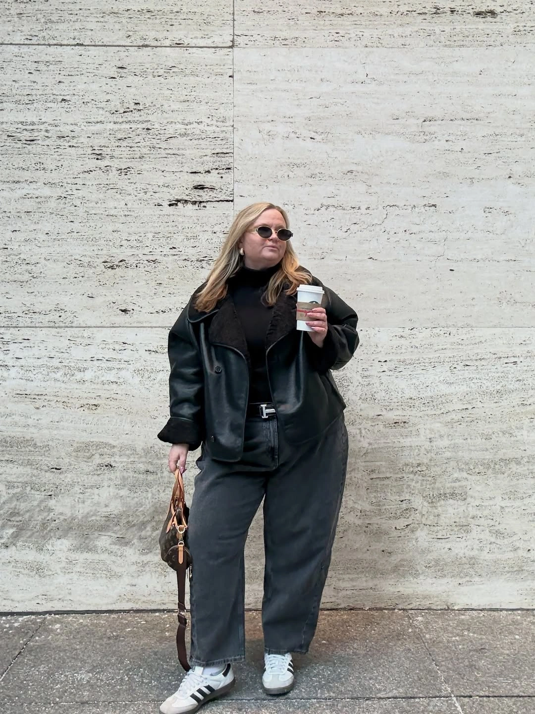 Black leather-look jacket with loose trousers and white sneakers