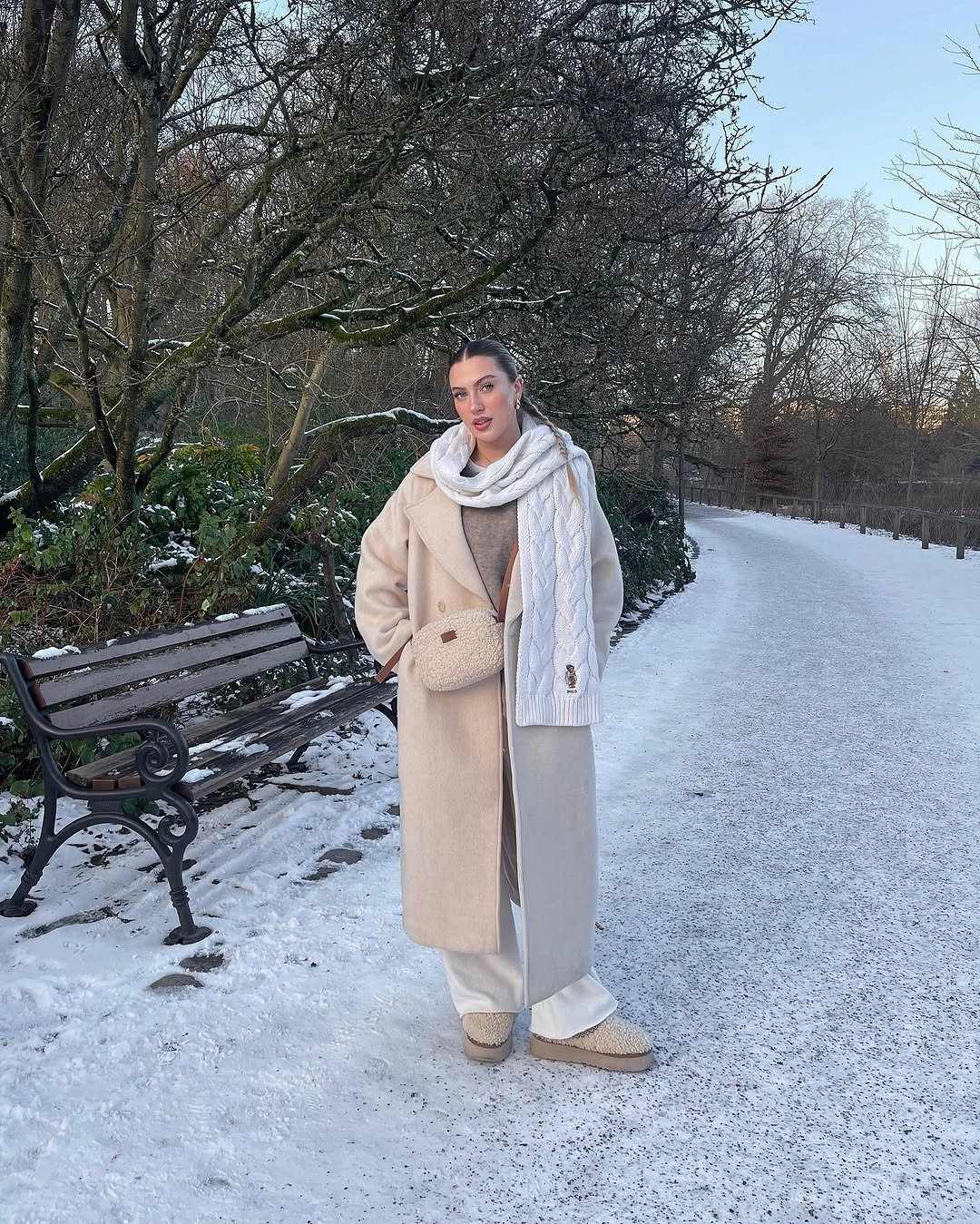 Long cream coat with pale scarf, relaxed trousers, and boots
