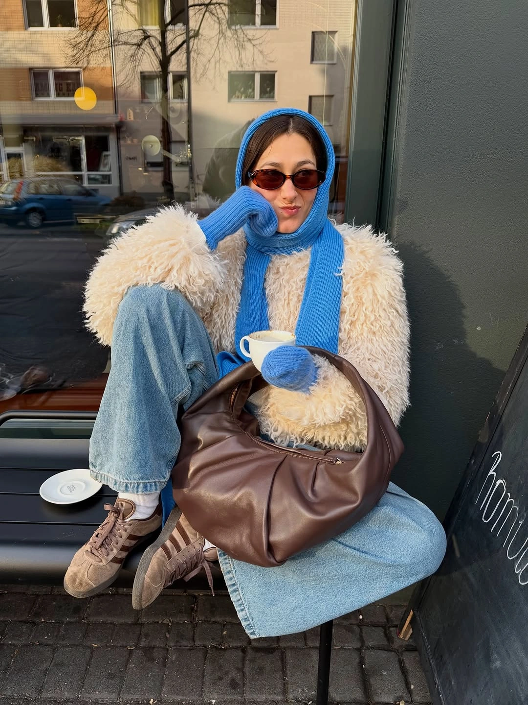 Cream fluffy vest with blue scarf, light jeans, and brown bag
