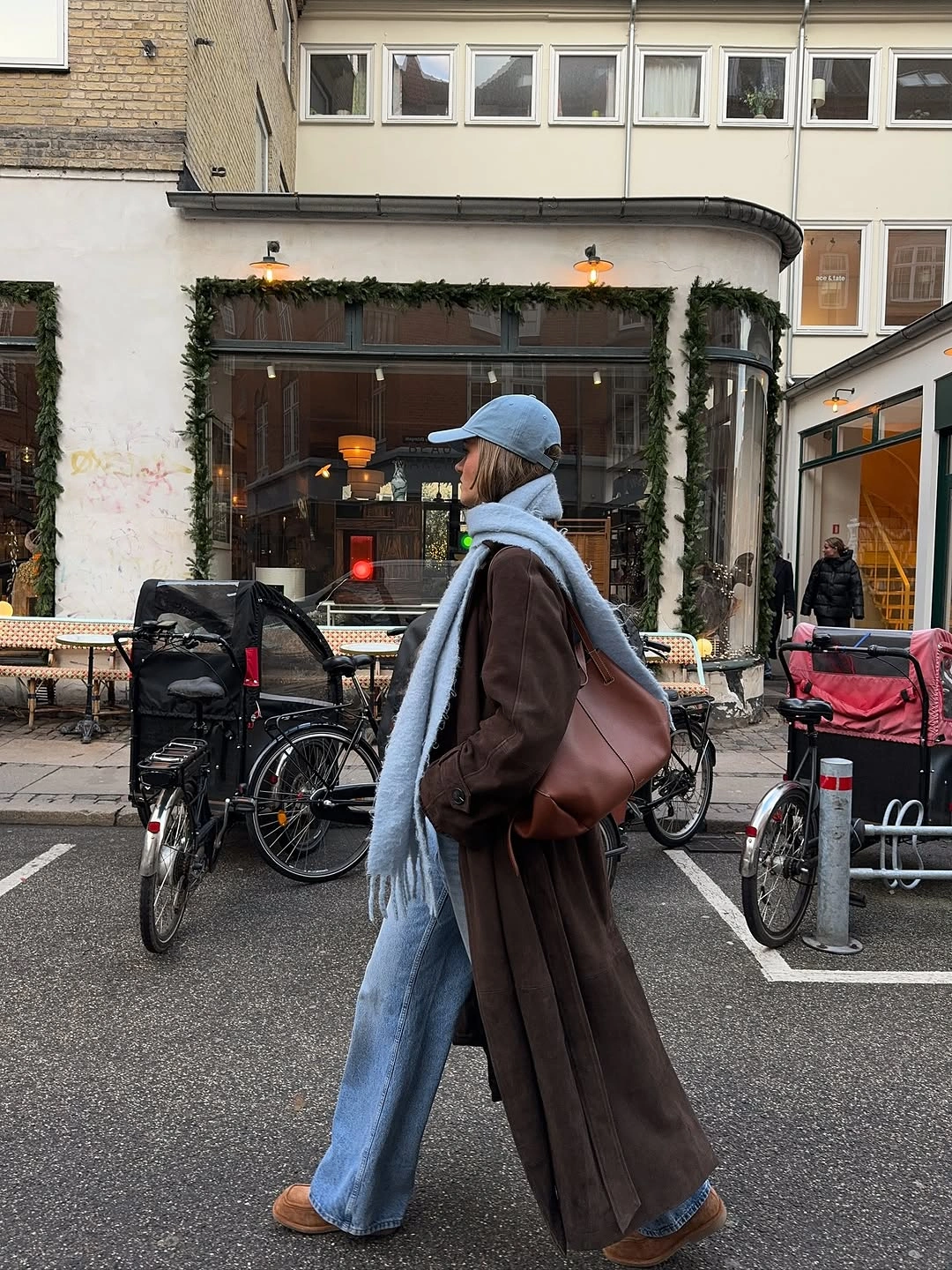 Long brown coat with light blue scarf, cap, and jeans