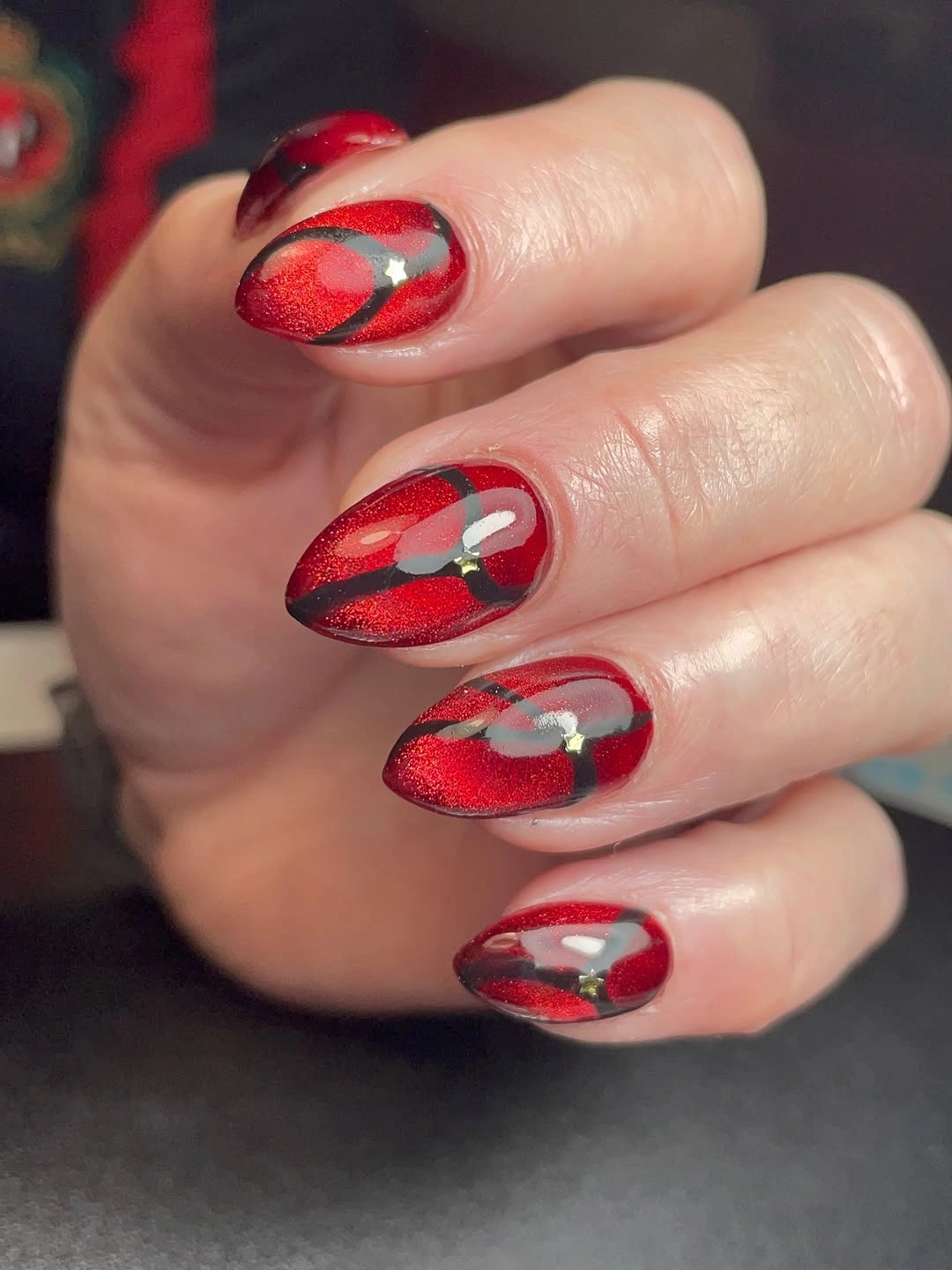 Almond red shimmer nails with dark curved accents and gold details