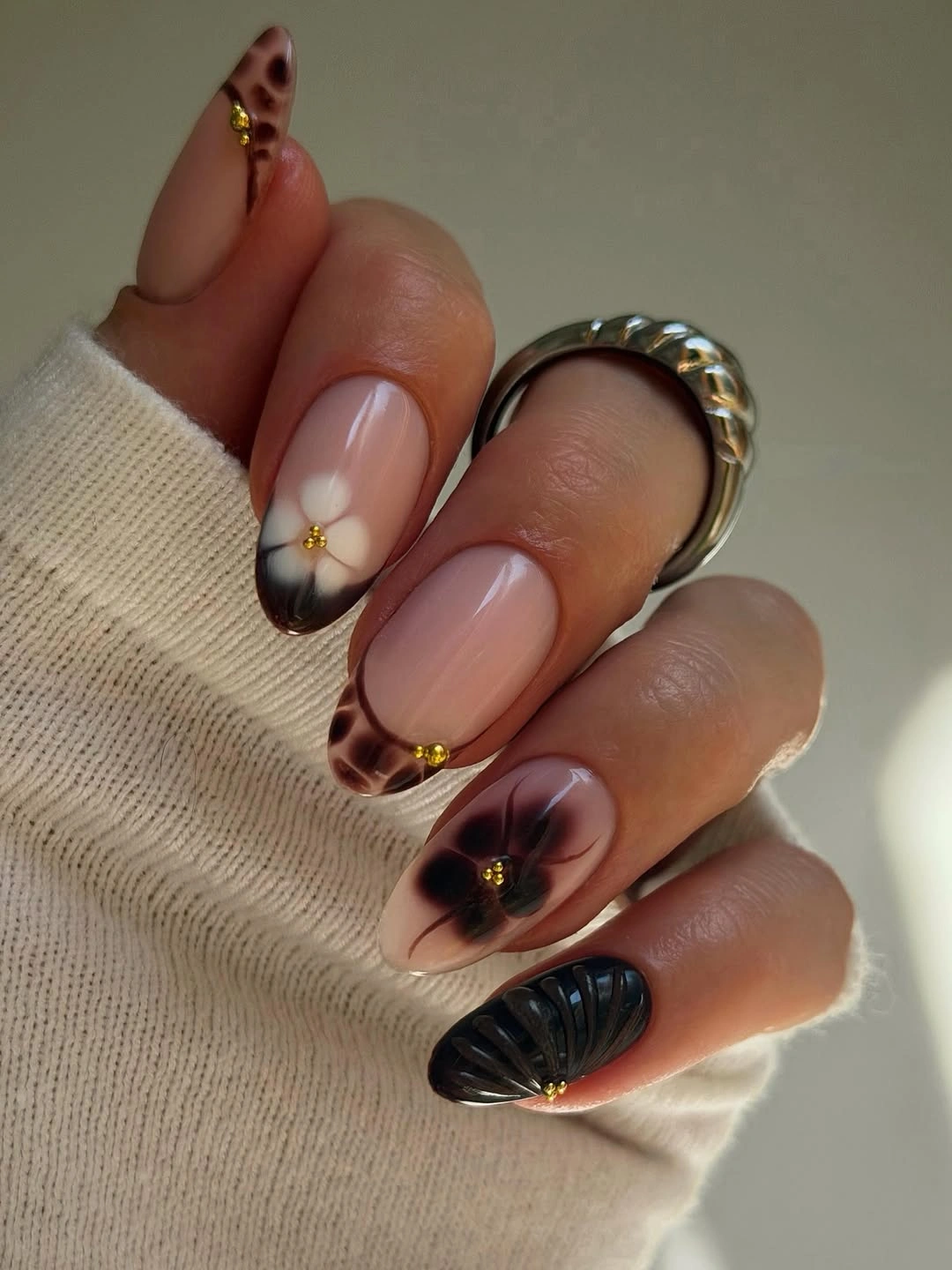 Almond nails with dark patterning, gold studs, and black texture